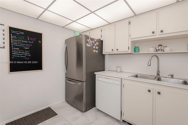 kitchen featuring a drop ceiling, white dishwasher, sink, stainless steel refrigerator, and white cabinetry