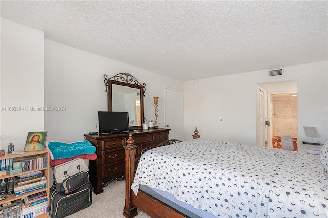 bedroom with a textured ceiling, light colored carpet, and ensuite bath