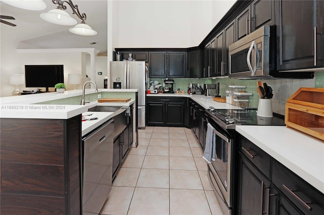 kitchen featuring appliances with stainless steel finishes, tasteful backsplash, light tile patterned floors, decorative light fixtures, and an island with sink