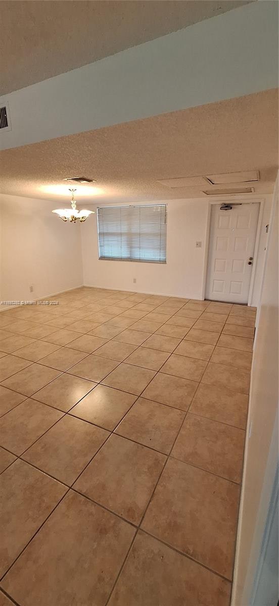 tiled spare room with a textured ceiling and a notable chandelier