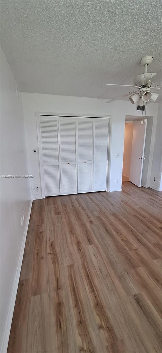 unfurnished bedroom with hardwood / wood-style floors, ceiling fan, a textured ceiling, and a closet