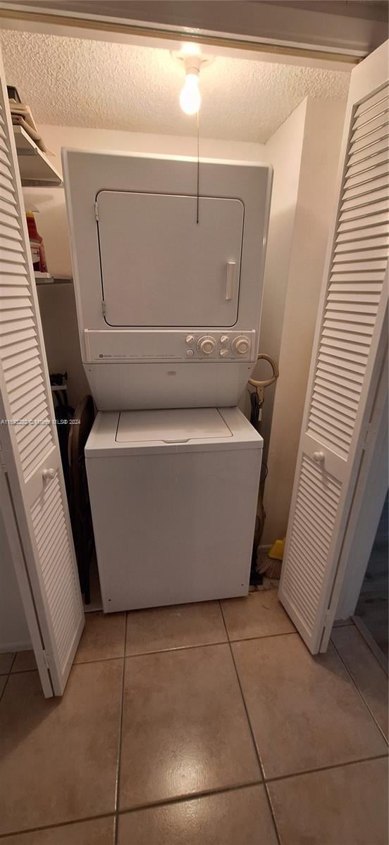 laundry area featuring light tile patterned floors, a textured ceiling, and stacked washer and dryer