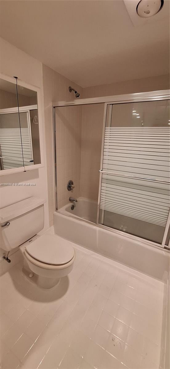 bathroom featuring combined bath / shower with glass door, tile patterned floors, and toilet