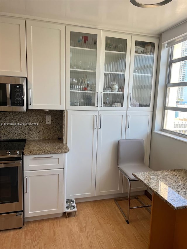 1833 S Ocean Dr Unit 1702, Hallandale Beach, FL 33009 - kitchen featuring appliances with stainless steel finishes, white cabinets, light wood-style flooring, light stone countertops, and glass insert cabinets