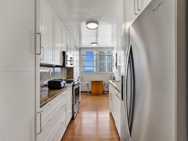 kitchen featuring tasteful backsplash, white cabinetry, appliances with stainless steel finishes, light wood-type flooring, and dark stone countertops