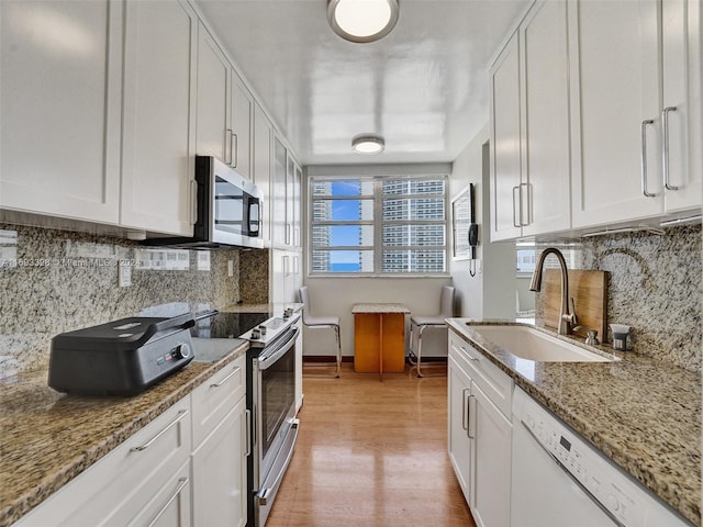 kitchen with stainless steel appliances, light stone counters, white cabinets, sink, and light wood-type flooring