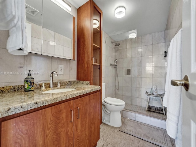 bathroom with tile walls, vanity, toilet, and tiled shower