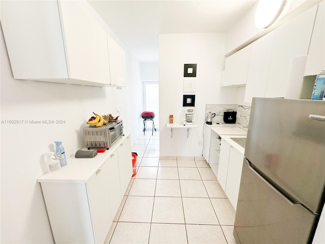 kitchen with stainless steel refrigerator, white cabinetry, and light tile patterned floors