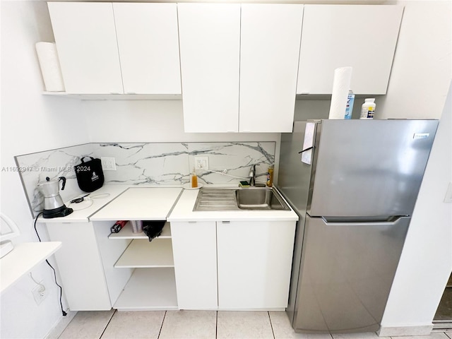 kitchen with white cabinets, light tile patterned flooring, stainless steel refrigerator, and sink