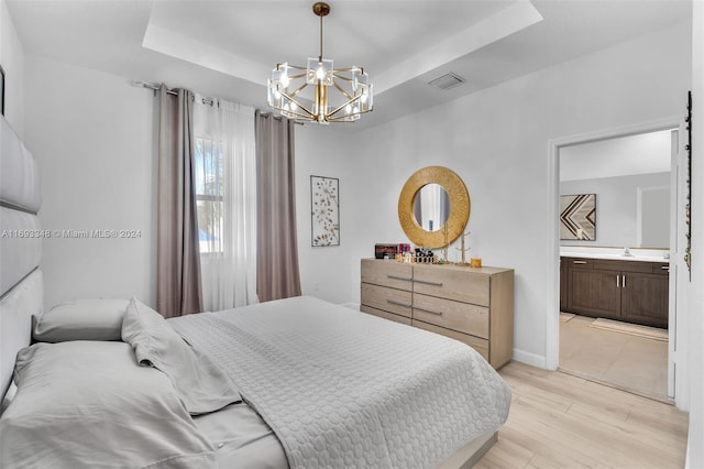 bedroom featuring ensuite bathroom, light hardwood / wood-style floors, a tray ceiling, and an inviting chandelier