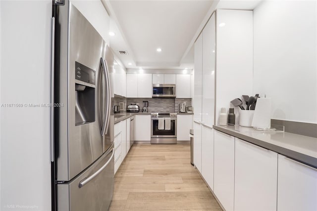 kitchen with white cabinets, decorative backsplash, light hardwood / wood-style floors, and stainless steel appliances