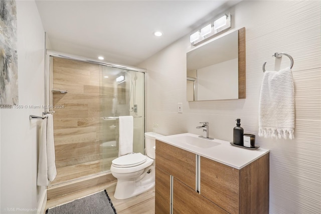 bathroom with toilet, a shower with door, tile walls, hardwood / wood-style floors, and vanity