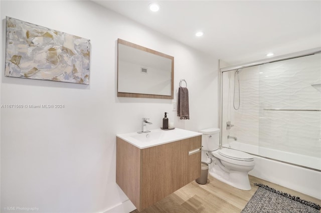 full bathroom featuring wood-type flooring, vanity, combined bath / shower with glass door, and toilet