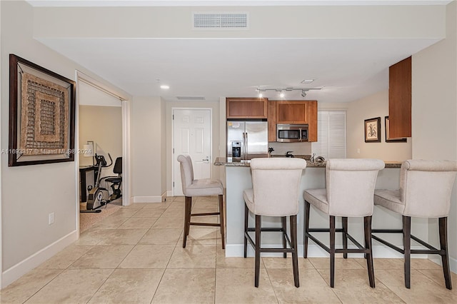 kitchen featuring light tile patterned flooring, a breakfast bar, kitchen peninsula, appliances with stainless steel finishes, and light stone countertops