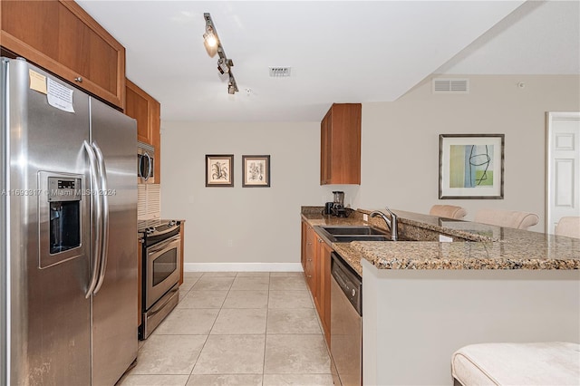 kitchen featuring light stone counters, appliances with stainless steel finishes, track lighting, a kitchen breakfast bar, and kitchen peninsula