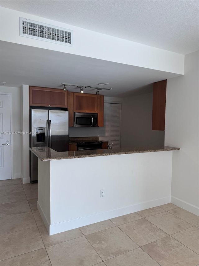 kitchen with stainless steel appliances, light tile patterned flooring, dark stone countertops, and kitchen peninsula