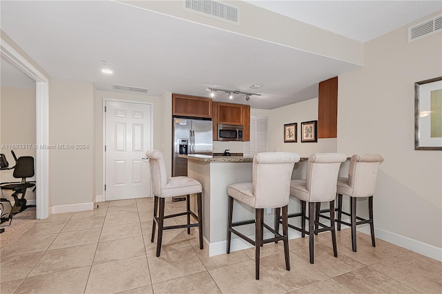 kitchen featuring a kitchen bar, light stone counters, kitchen peninsula, light tile patterned flooring, and appliances with stainless steel finishes