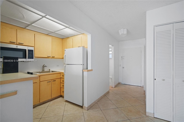 kitchen with light tile patterned floors, sink, white refrigerator, and light brown cabinets