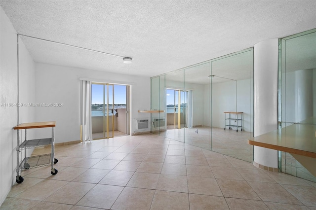 tiled empty room with an AC wall unit, a water view, and a textured ceiling