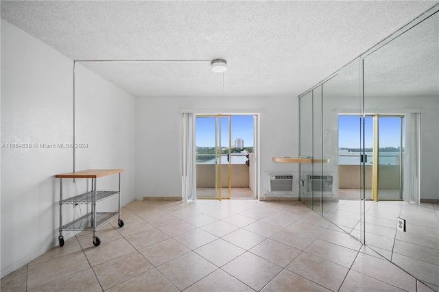 spare room featuring a water view, a textured ceiling, light tile patterned floors, and a wall mounted air conditioner