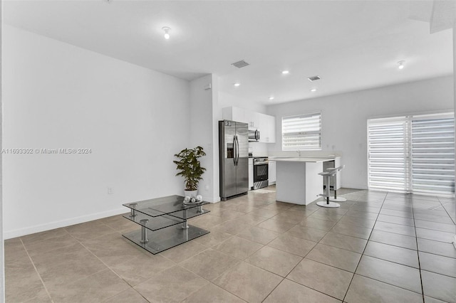 kitchen with a center island, white cabinets, a breakfast bar area, light tile patterned floors, and stainless steel appliances