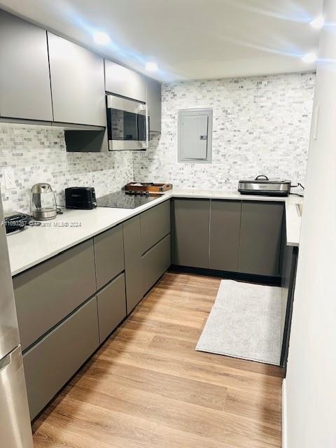 kitchen featuring electric panel, black electric cooktop, tasteful backsplash, gray cabinetry, and light wood-type flooring