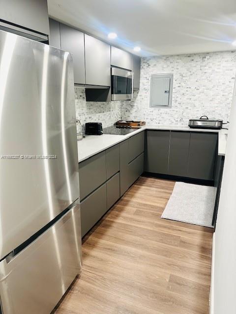 kitchen with stainless steel appliances, light hardwood / wood-style floors, tasteful backsplash, electric panel, and gray cabinets