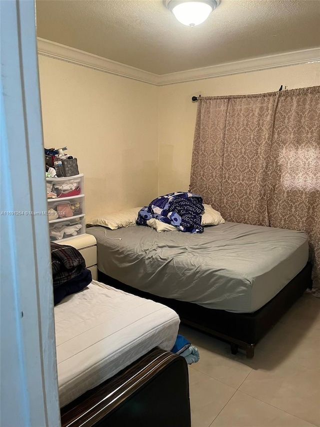 bedroom with a textured ceiling, light tile patterned floors, and ornamental molding