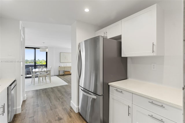 kitchen with light stone countertops, white cabinetry, appliances with stainless steel finishes, and light wood-type flooring