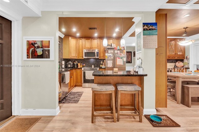 kitchen with a kitchen bar, tasteful backsplash, stainless steel appliances, light hardwood / wood-style floors, and hanging light fixtures