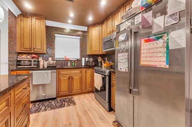 kitchen with dark stone countertops, crown molding, light hardwood / wood-style floors, decorative backsplash, and appliances with stainless steel finishes