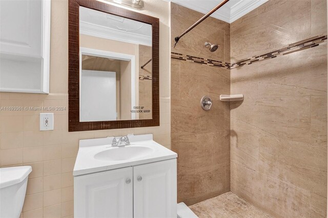 bathroom featuring vanity, toilet, ornamental molding, tile walls, and a tile shower