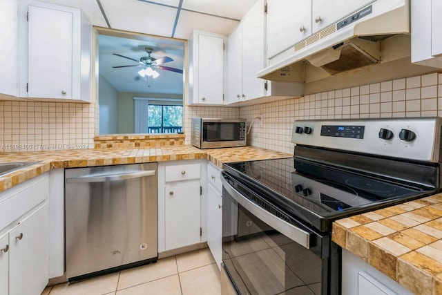 kitchen with tasteful backsplash, stainless steel appliances, ceiling fan, white cabinets, and light tile patterned flooring