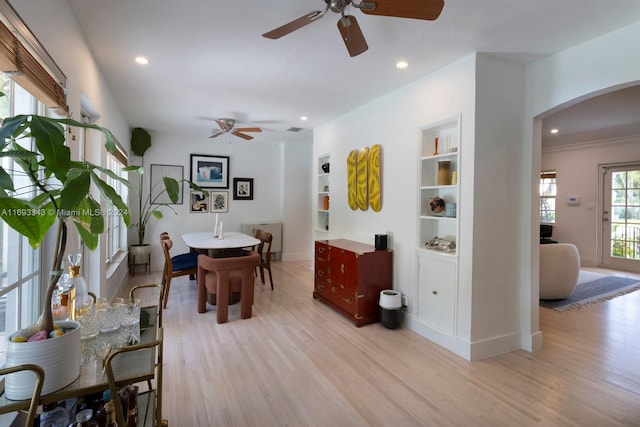 dining area with ceiling fan, built in features, ornamental molding, and light wood-type flooring