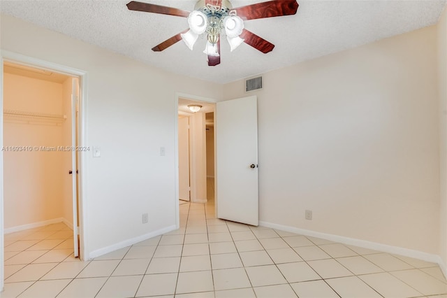 unfurnished bedroom with a textured ceiling, a closet, a spacious closet, and ceiling fan