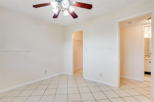 empty room with ceiling fan, light tile patterned floors, and a textured ceiling