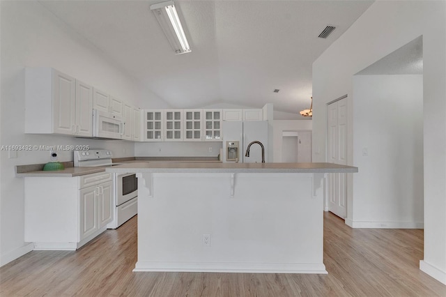 kitchen with lofted ceiling, white appliances, a breakfast bar, white cabinetry, and light wood-style floors