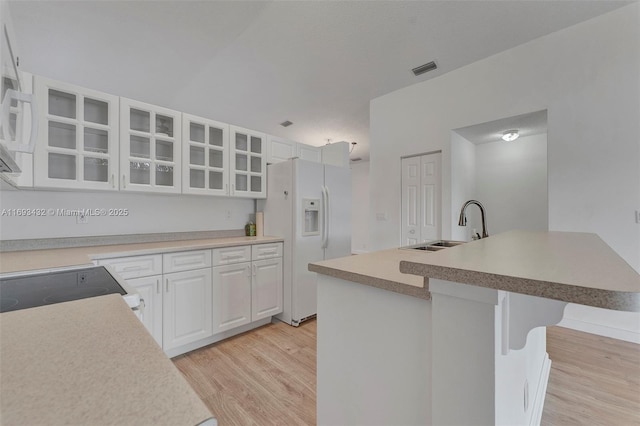 kitchen featuring light wood finished floors, white refrigerator with ice dispenser, white cabinets, glass insert cabinets, and a sink