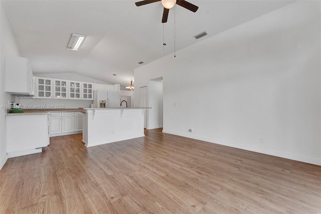 unfurnished living room featuring light wood finished floors, visible vents, vaulted ceiling, ceiling fan, and baseboards