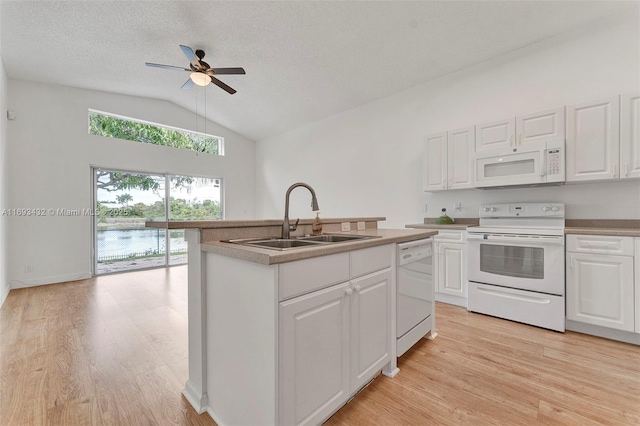 kitchen with light wood finished floors, lofted ceiling, white cabinets, a sink, and white appliances