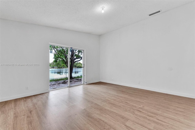 spare room with light wood-type flooring, visible vents, and a textured ceiling