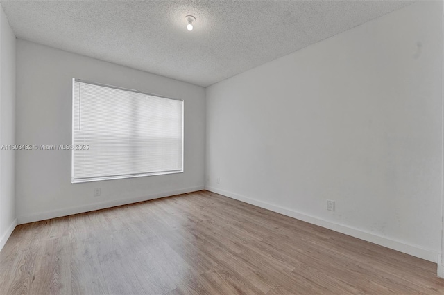 spare room with a textured ceiling, wood finished floors, and baseboards