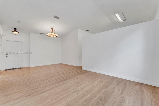 empty room featuring a notable chandelier, visible vents, a textured ceiling, light wood-type flooring, and baseboards