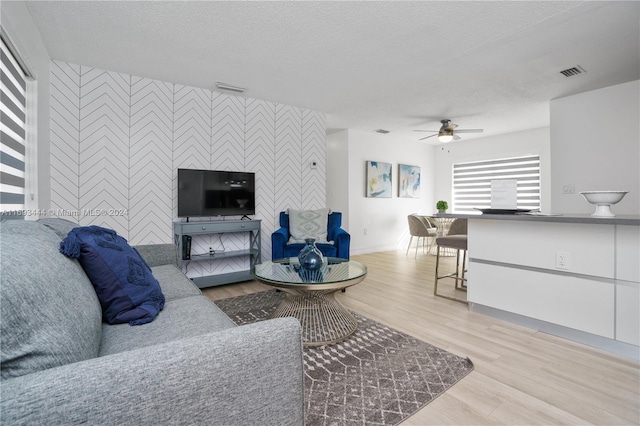 living room featuring ceiling fan, light hardwood / wood-style floors, and a textured ceiling