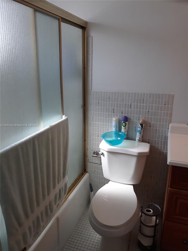 full bathroom featuring shower / bath combination with glass door, vanity, toilet, and tile walls