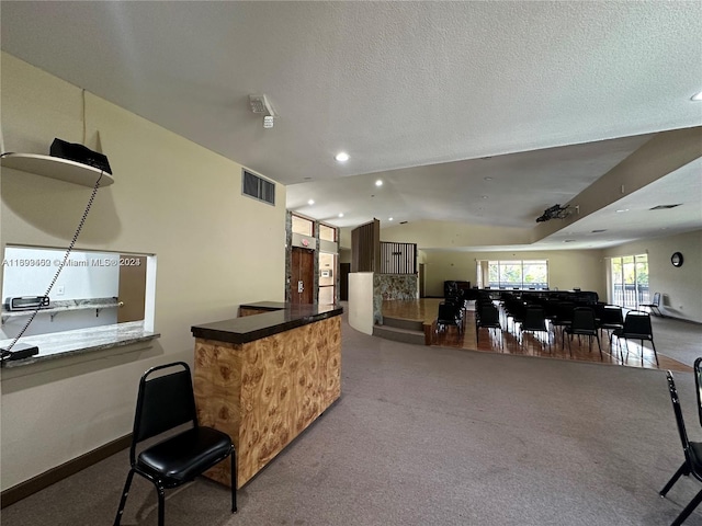 interior space featuring kitchen peninsula, a textured ceiling, lofted ceiling, and carpet flooring