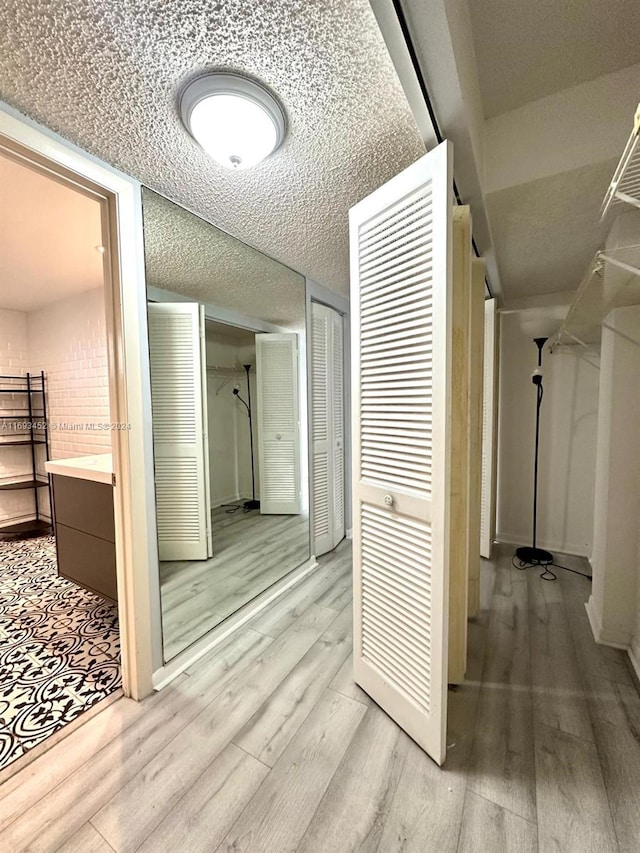 hall featuring light wood-type flooring, a textured ceiling, and brick wall