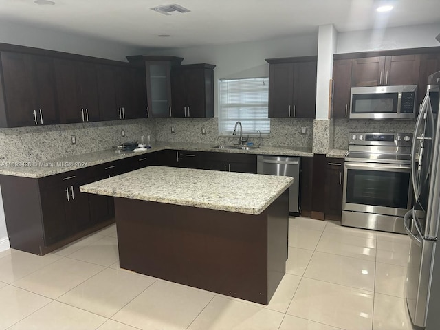 kitchen with a kitchen island, appliances with stainless steel finishes, light tile patterned floors, decorative backsplash, and sink