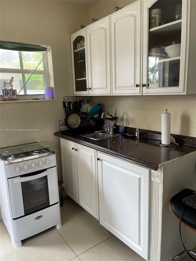 kitchen featuring dark stone counters, white cabinetry, white gas range, light tile patterned floors, and sink