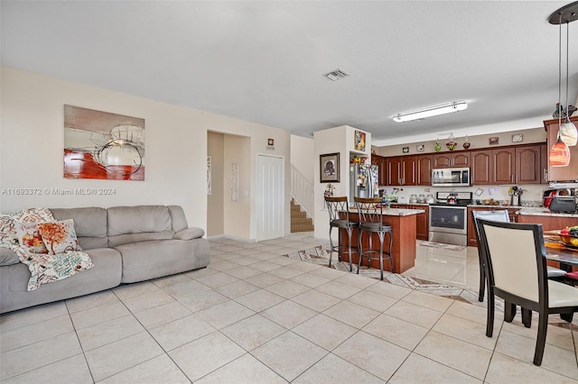 kitchen with hanging light fixtures, light tile patterned floors, a kitchen breakfast bar, a kitchen island, and appliances with stainless steel finishes